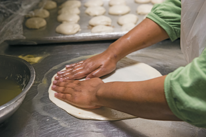 Refugee working in the kitchen flattening out bread to cook with.