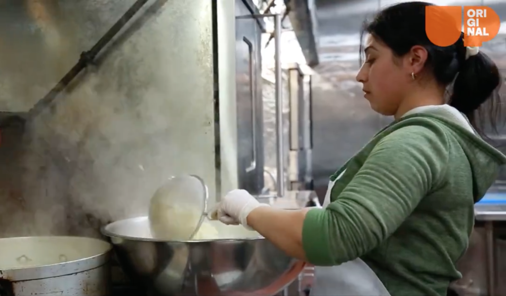 Refugee worker for Eat Offbeat cooking in the kitchen in a big bowl with a ladle.